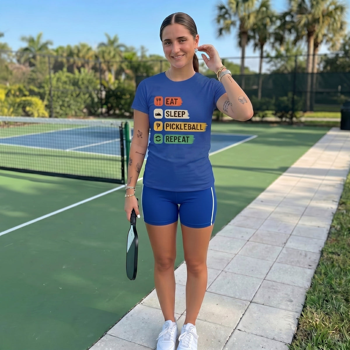  blue cotton pickleball t-shirt with Eat Sleep Pickleball Repeat graphic worn by a woman on a court.