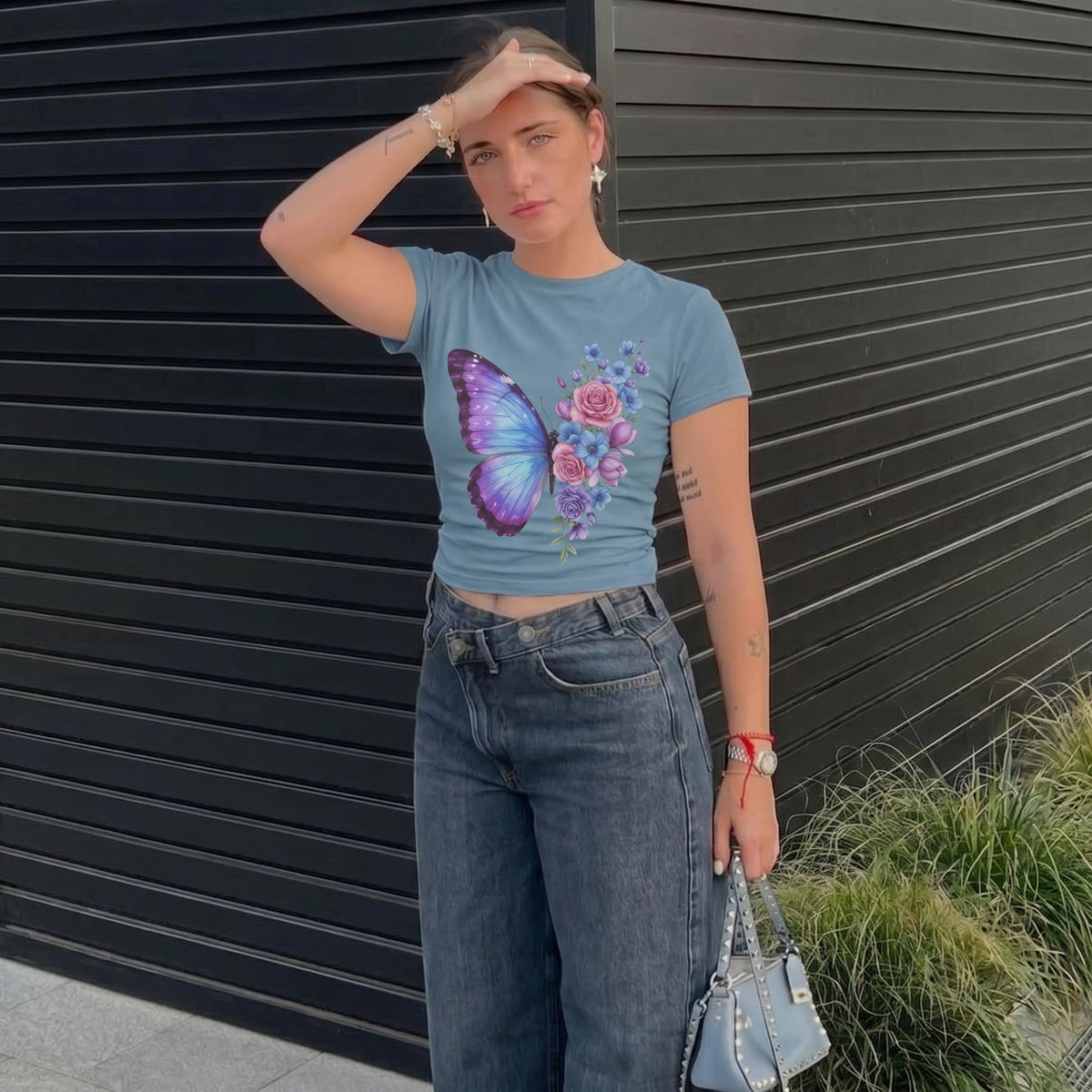  women's blue micro rib baby tee featuring a pastel butterfly and floral print, worn with dark jeans.
