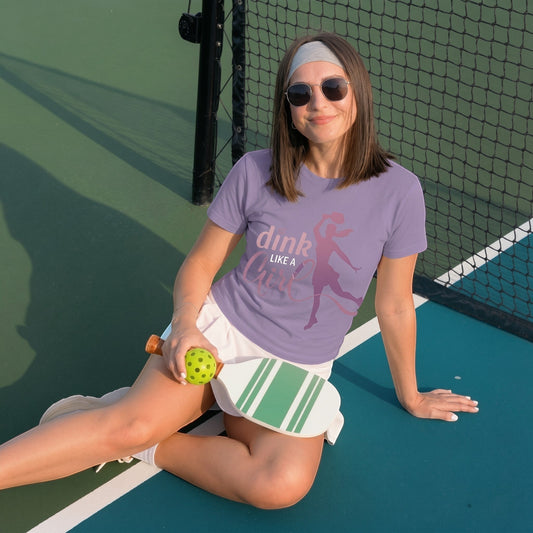  lavender short sleeve cotton tee with Dink Like a Girl pickleball graphic worn by a woman on a court.