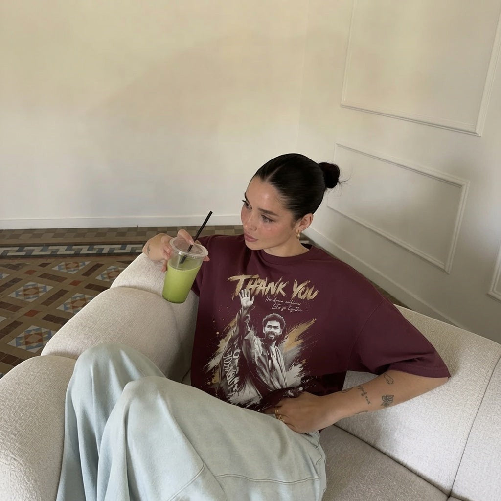  maroon oversized cotton tribute tee with goalkeeper graphic print worn by a woman on a white sofa.