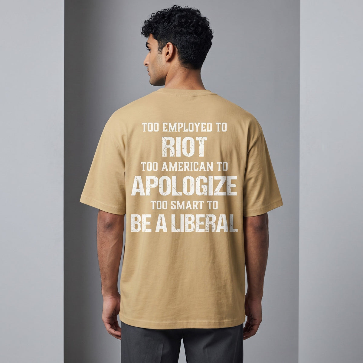  tan oversized t-shirt with white distressed text print on the back, worn by a man from behind.